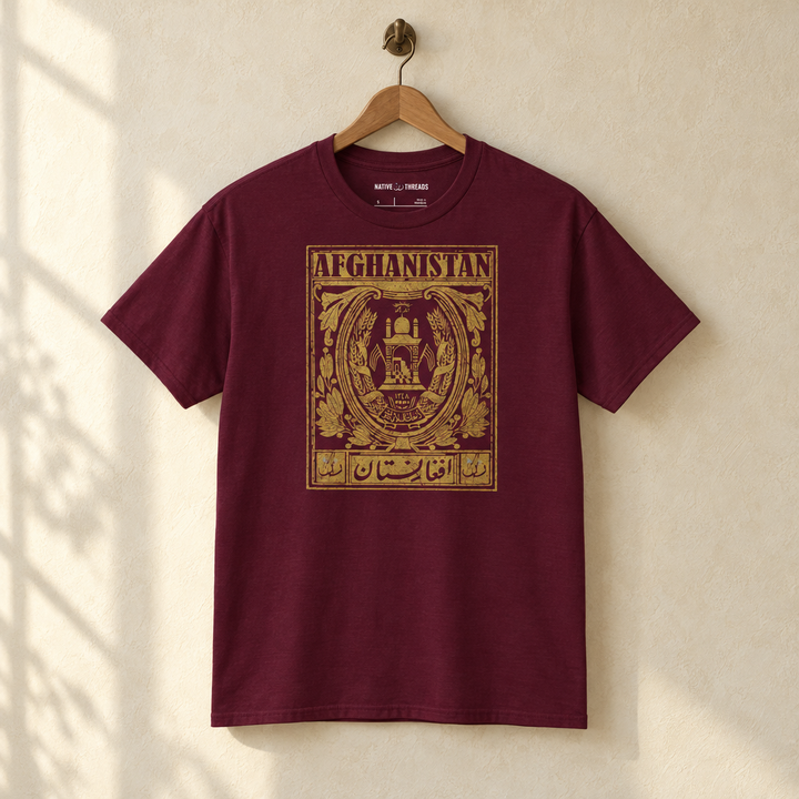 Afghanistan Postcard T-shirt, hanging on a wooden hanger against a pale wall.