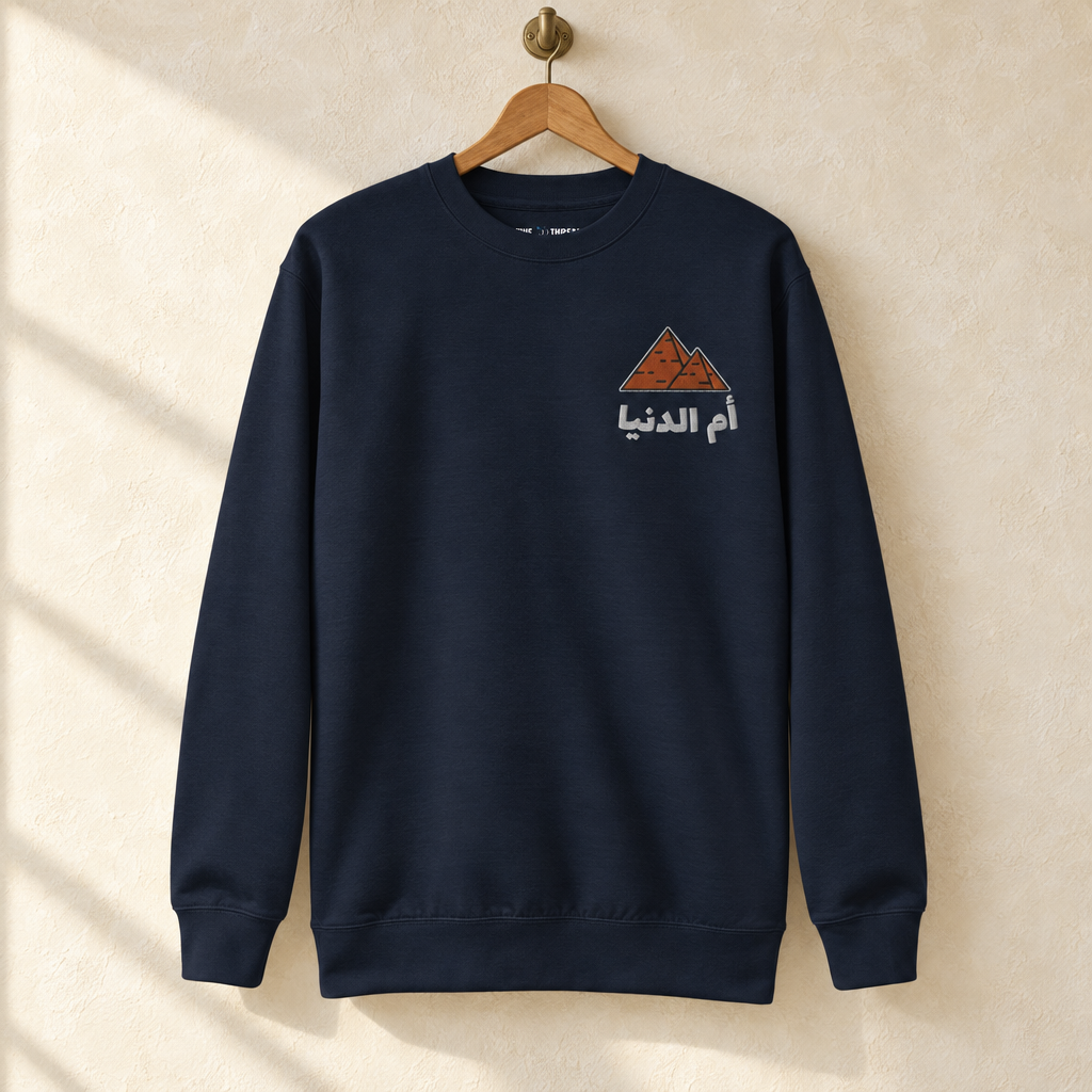 Egypt Umm El Dunya Sweater, hanging on a wooden hanger against a pale wall.