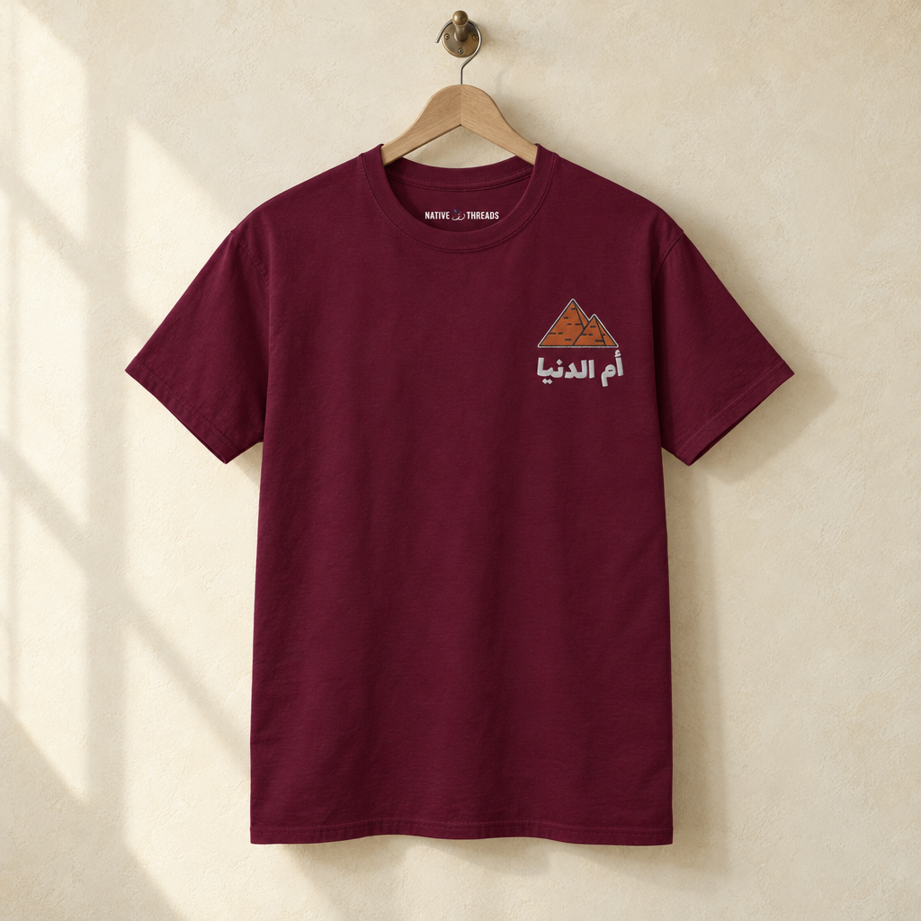Egypt Umm El Dunya T-shirt, hanging on a wooden hanger against a pale wall.