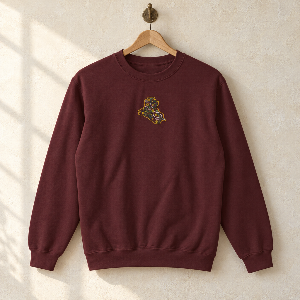 Maroon Iraq sweater with a floral map of Iraq embroidered on the chest, hanging on a wooden hanger.