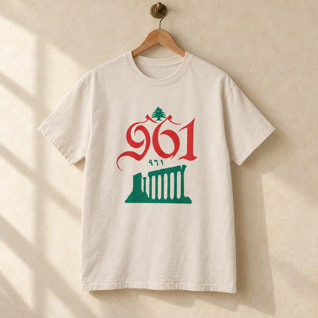 Lebanon Baalbek Area Code T-shirt, hanging on a wooden hanger against a pale wall.