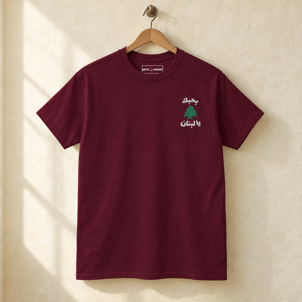 Lebanon Cedar Tree T-shirt, hanging on a wooden hanger against a pale wall.