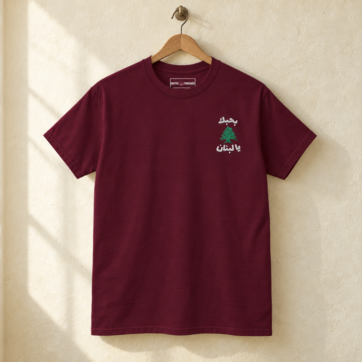 Lebanon Cedar Tree T-shirt, hanging on a wooden hanger against a pale wall.