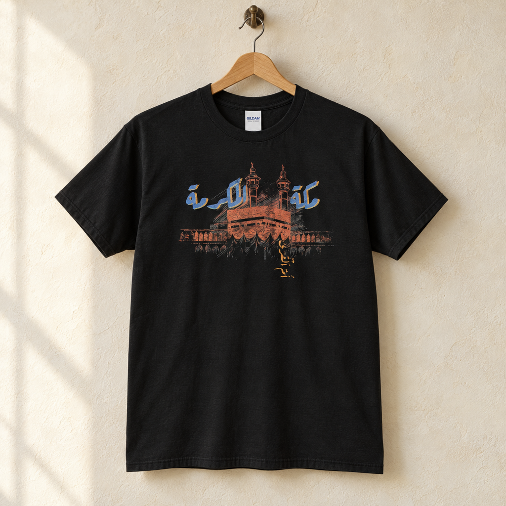 Makkah Al Mukarramah T-shirt, hanging on a wooden hanger against a pale wall.