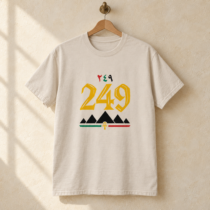 Sudan Pyramid Area Code T-shirt, hanging on a wooden hanger against a pale wall.