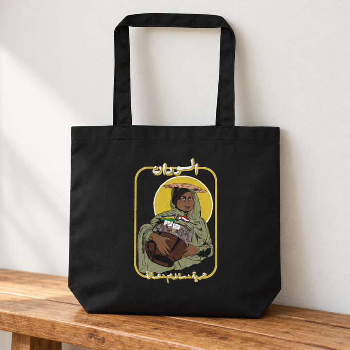 Sudan Revolution Tote Bag, standing on a wooden bench with the printed front visible.